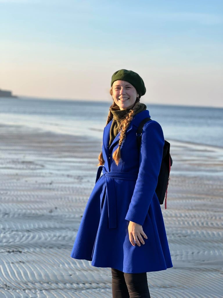 na fotce stojím na pláži v Lotyšsku, na sobě mám modrý kabát a zelený baret