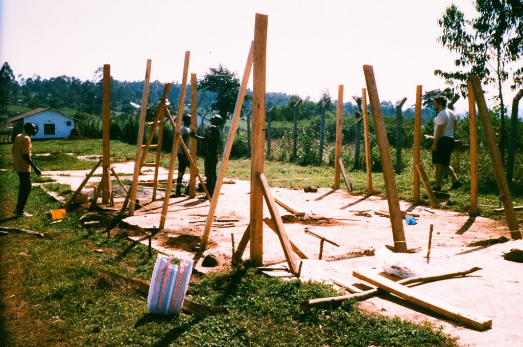 Staveniště dílny. Přibližně dvoumetrové latě jsou připravené ve vyhloubených dírách a čekají na zabetování.